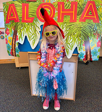 a girl dressed in Hawaiian costume standing in front of a sign that says Aloha