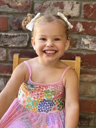 girl in pink dress sitting in a chair and smiling