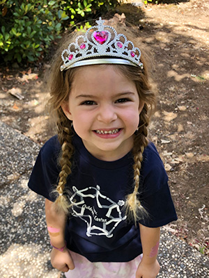 preschool student wearing a tiara and a childrens center tshirt smiling at the camera